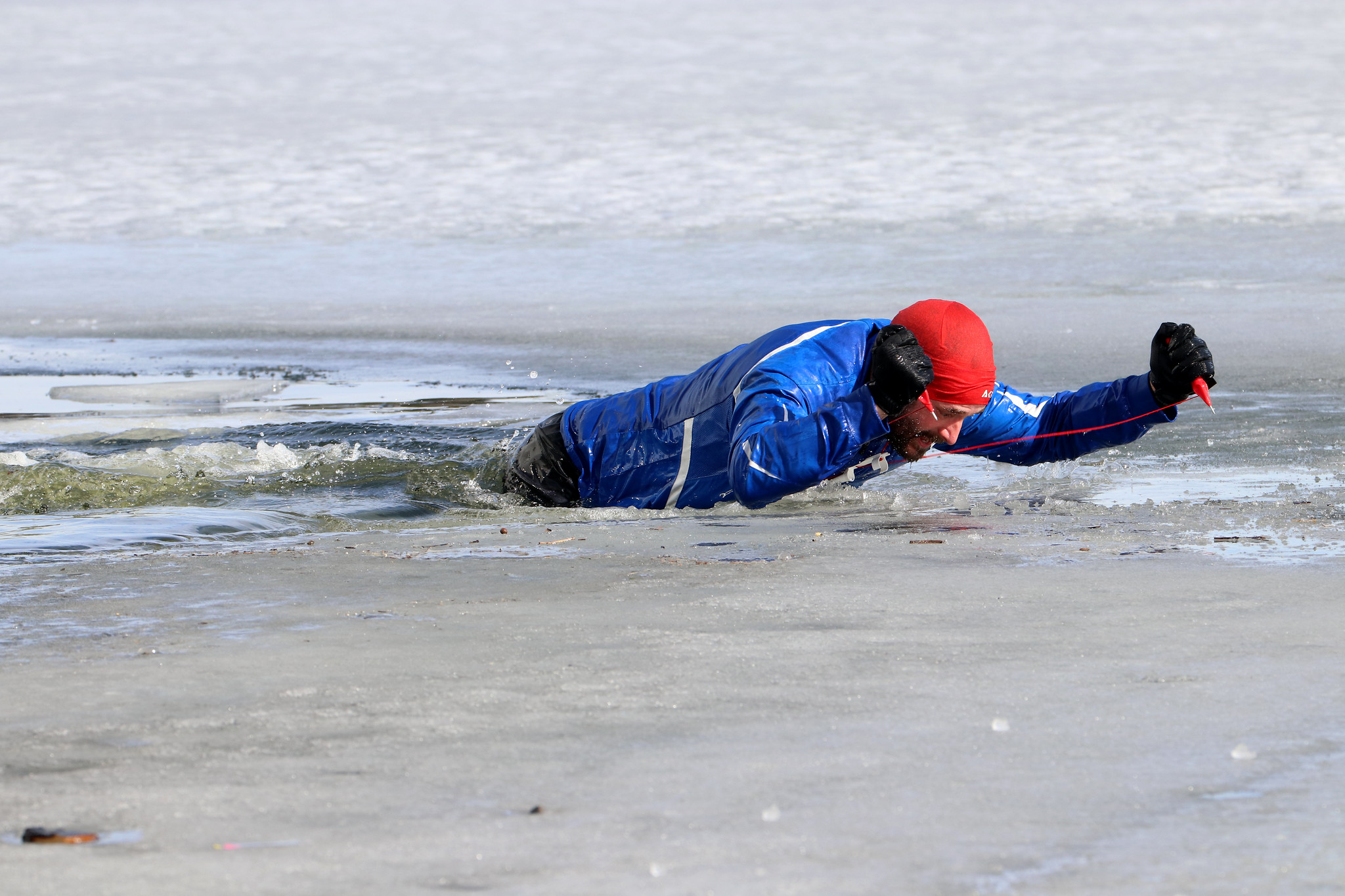 En mann prøver å komme seg opp på isen ved hjelp av ispigger. 